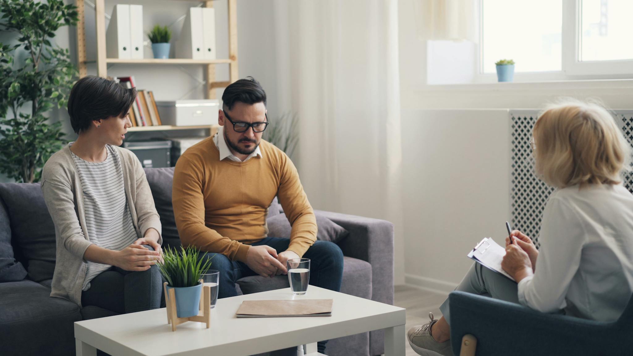 A couple in a psychotherapy session with a therapist in a cozy office.