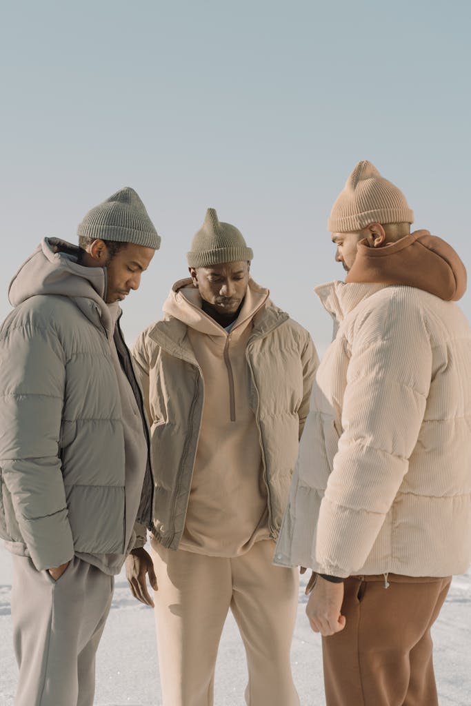 Three men in winter clothing featuring stylish puffer jackets and knit hats under clear sky.